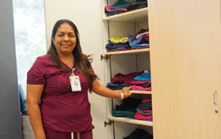 Athena Alvarado stands beside shelves of medical scrubs.